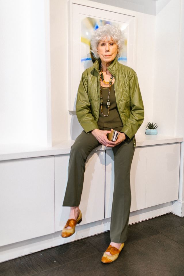 Woman in an olive jacket and trousers seated by a window