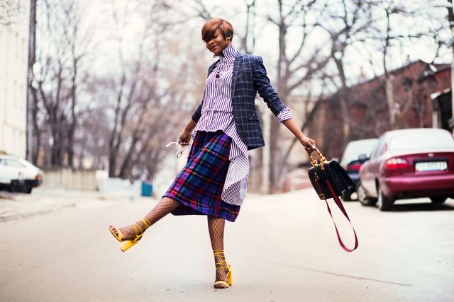 Woman mid-stride on a street in a plaid blazer and pleated skirt